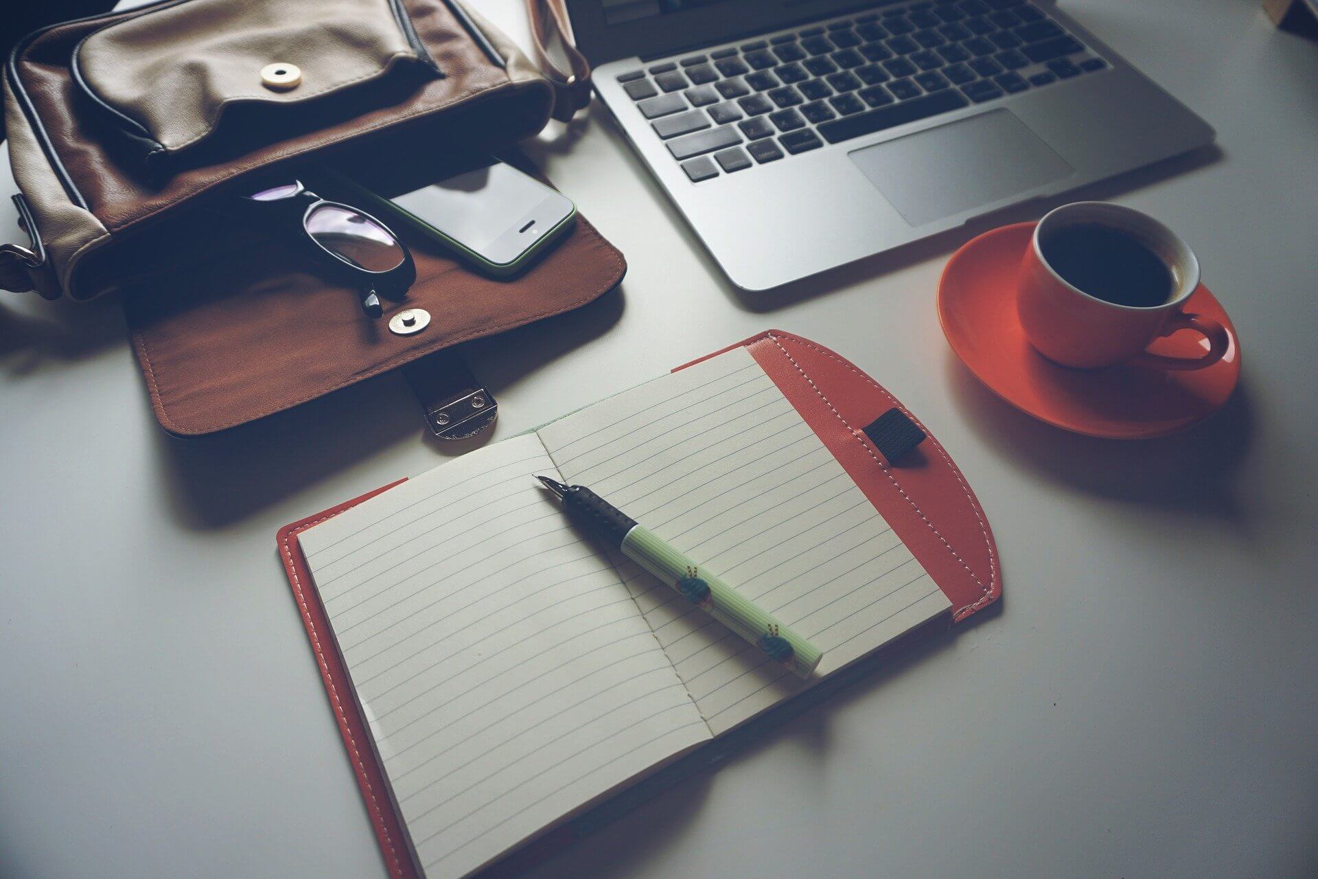 A notebook, a phone, and a cup of coffee on a desk.